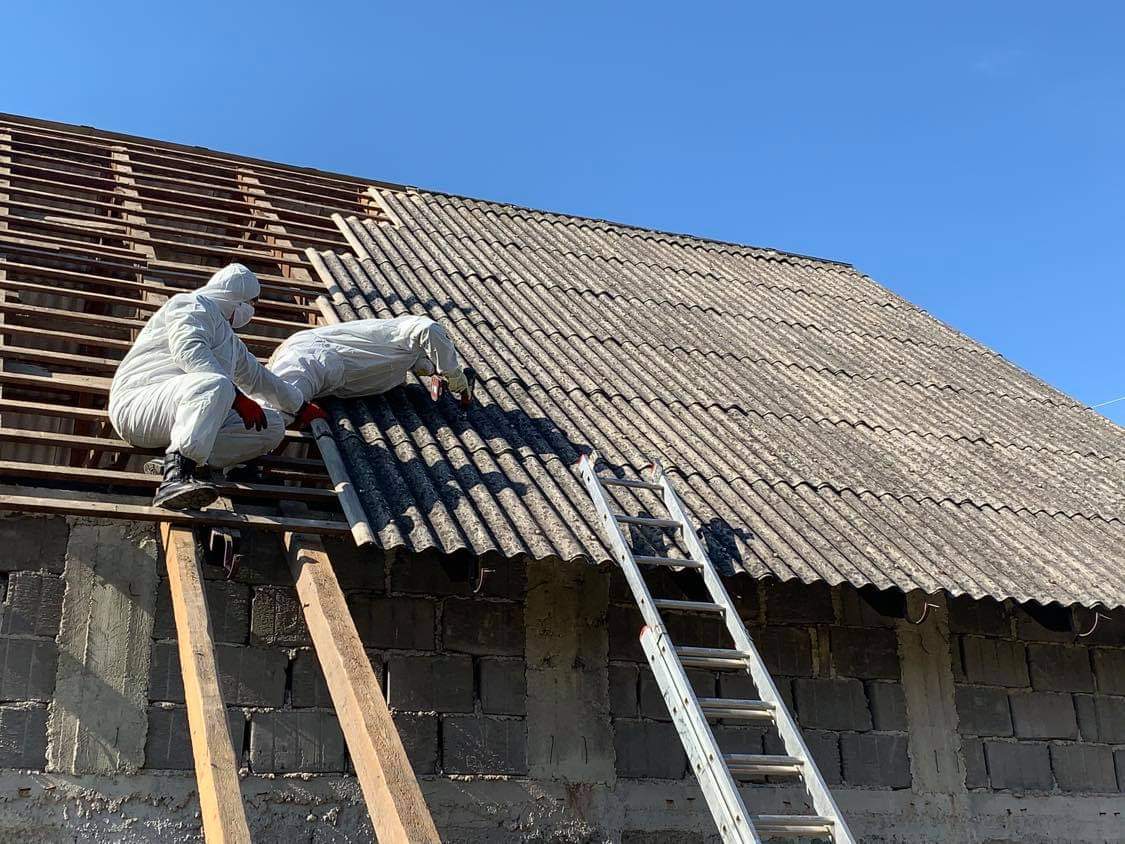 Pracovníci v ochranných oblekoch demontujú azbestovú strešnú krytinu